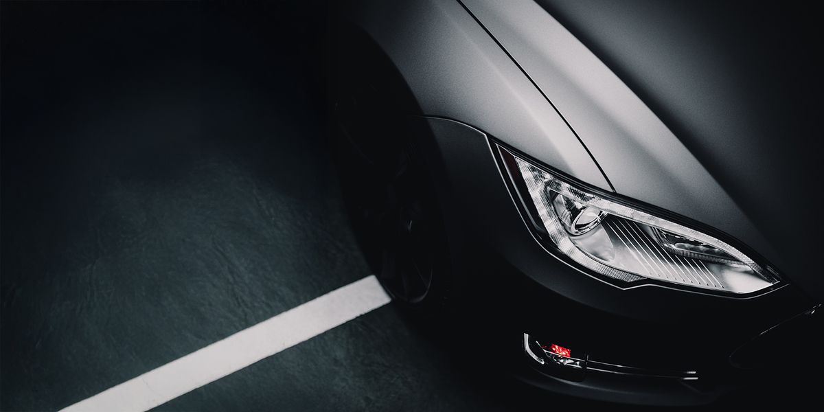 Im Bild ist ein schwarzes Auto von oben zu sehen, das in der Dunkelheit steht, mit nur schwachem Licht, das es umgibt