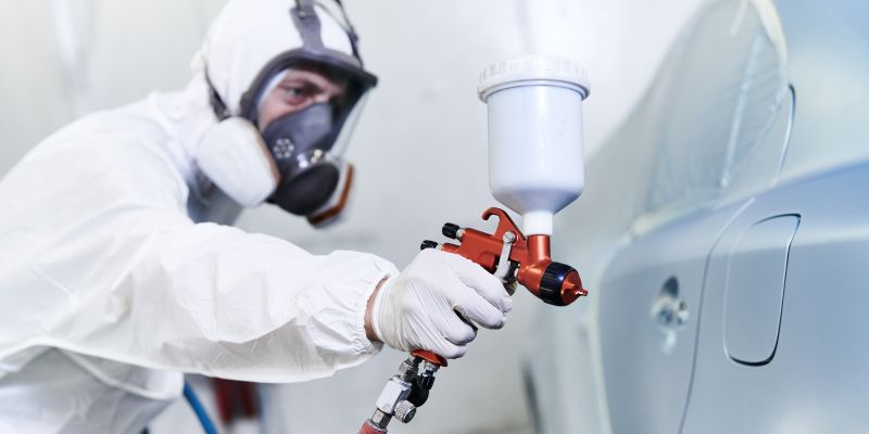 Eine Person im Anzug lackiert ein Auto