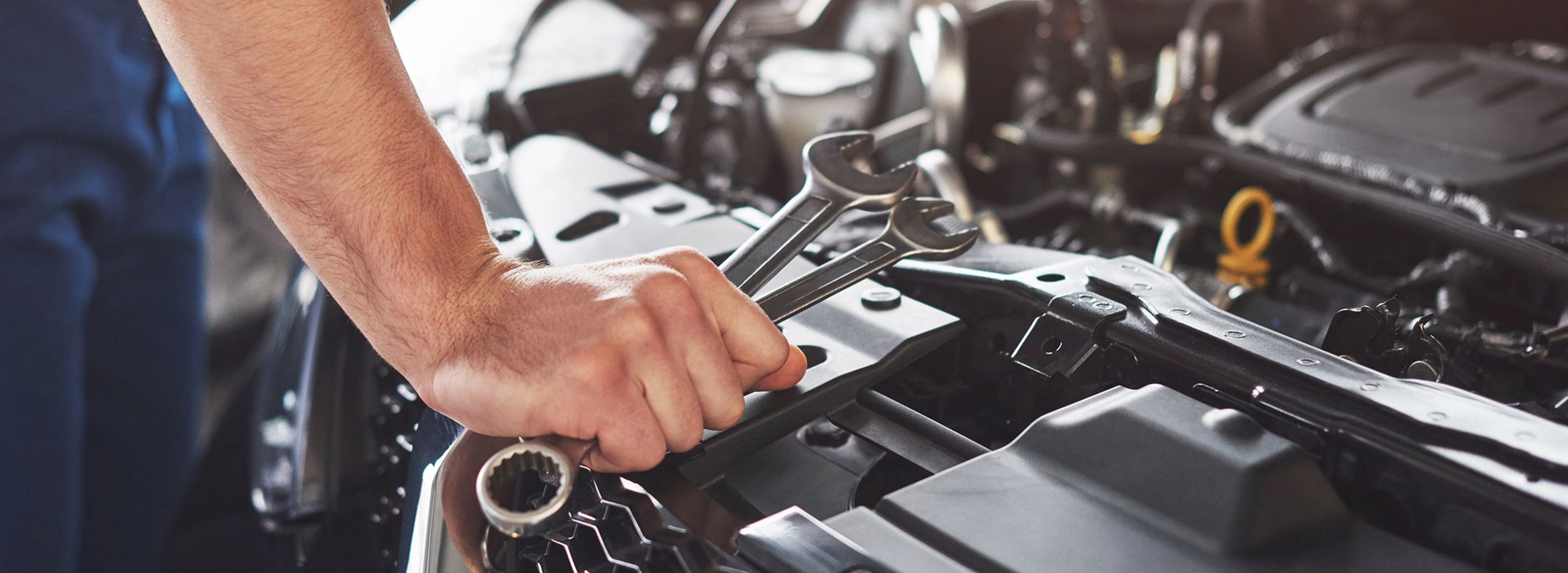 Ein Mann mit Schraubenschlüsseln in der Hand arbeitet an dem Motor eines Fahrzeugs